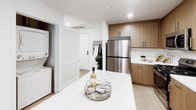 Located at 1446 Tamarind Ave in the heart of Hollywood, Los Angeles, this thoughtfully designed single-floor residence offers a clean, modern aesthetic throughout. Light hardwood flooring runs continuously across the space, complementing the soft, neutral color palette accented by sage green walls that add a calming warmth.

The open-concept living area is filled with natural light streaming through floor-to-ceiling vertical blinds, creating a bright and welcoming atmosphere. The space accommodates both a dining area and a lounge corner, with curated décor including abstract wall art and contemporary furnishings.

The kitchen is a standout feature, outfitted with warm natural wood cabinetry, white quartz countertops, a white subway tile backsplash, and a full suite of stainless steel appliances including a gas range, microwave, and refrigerator. A kitchen island provides additional prep and entertaining space. A stacked in-unit washer and dryer is conveniently tucked nearby.

The bedroom is a tranquil retreat, featuring sage green accent walls, light hardwood flooring, and direct access to the bathroom. The bathroom is elegantly appointed with marble-look tile surrounding a deep soaking tub and sliding glass shower enclosure, paired with warm wood cabinetry and modern fixtures. Recessed lighting throughout the space enhances its polished, contemporary feel.