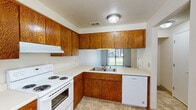 This single-story home offers a practical and efficient layout across three bedrooms, one bathroom, a living room, kitchen, and connecting hallways. The kitchen is a standout feature, outfitted with warm oak cabinetry spanning both upper and lower sections, light-toned countertops, and white appliances including an electric range, dishwasher, and refrigerator. A window above the sink allows natural light to filter in and provides a view of the surrounding greenery outside. The tile-style flooring in the kitchen adds durability and ease of maintenance. Each of the three bedrooms is finished with wall-to-wall carpet, providing a comfortable feel underfoot. The bedrooms are bright and well-proportioned, with windows dressed in horizontal blinds and ceiling fans with integrated lighting for year-round comfort. Closet storage is available in the bedrooms, including sliding-door closets with built-in shelving and hanging rods. Textured ceilings are consistent throughout the home, lending a classic residential character. Three hallways connect the rooms efficiently, contributing to a logical flow throughout the floor plan. The exterior is set within a tree-lined neighborhood, offering a quiet and established residential setting. Overall, the home presents a clean, functional living environment well-suited for everyday needs.