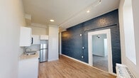 This 380 square foot, single-floor apartment offers a thoughtful blend of style and functionality. The space comprises one bedroom, one bathroom, and a well-equipped kitchen, all designed to maximize efficiency in a compact layout. The bedroom, measuring 130 square feet, features a striking blue ombre brick wall, adding a contemporary touch to the space. Wood-look flooring throughout provides warmth and continuity.

The kitchen is a highlight, boasting white Shaker-style cabinets, stainless steel appliances, and a sleek countertop. It includes a range, microwave, dishwasher, and refrigerator, all neatly integrated to optimize the available space. The bathroom showcases a modern design with large format marble-look tiles, a combination tub-shower, and crisp white fixtures.

Recessed lighting and strategically placed wall sconces contribute to the apartment's bright and airy feel. The unit's design cleverly balances aesthetics with practicality, making it an ideal space for urban living. Despite its compact size, the apartment offers a comfortable and stylish environment, perfect for singles or couples seeking a contemporary living space.