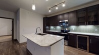 This single-floor residence showcases a contemporary design with carefully selected finishes throughout. The kitchen serves as the focal point of the space, centered around a substantial island topped with striking granite countertops and an undermount sink with a sleek chrome faucet. Pendant lighting and track lights illuminate the workspace, while floor-to-ceiling dark espresso cabinetry provides generous storage. A herringbone-patterned tile backsplash with subtle iridescent tones adds visual interest, and a full suite of stainless steel appliances — including a range, microwave, refrigerator, and dishwasher — completes the culinary space. Rich hardwood-style flooring flows through the main living areas, adding warmth and continuity.

The bedrooms offer a more relaxed atmosphere, featuring neutral carpet, ceiling fans, and windows fitted with blinds that allow controlled natural light. The bathrooms are finished with large-format neutral floor tiles, dark vanity cabinetry with marble-style countertops, framed mirrors, and ample overhead storage. The primary bathroom includes a glass-enclosed walk-in shower with tile surround, while a secondary bathroom provides additional convenience. Overall, the space presents a cohesive modern aesthetic with quality finishes throughout.