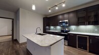 This single-floor residence showcases a contemporary design with carefully selected finishes throughout. The kitchen serves as the focal point of the space, centered around a substantial island topped with striking granite countertops and an undermount sink with a sleek chrome faucet. Pendant lighting and track lights illuminate the workspace, while floor-to-ceiling dark espresso cabinetry provides generous storage. A herringbone-patterned tile backsplash with subtle iridescent tones adds visual interest, and a full suite of stainless steel appliances — including a range, microwave, refrigerator, and dishwasher — completes the culinary space. Rich hardwood-style flooring flows through the main living areas, adding warmth and continuity.

The bedrooms offer a more relaxed atmosphere, featuring neutral carpet, ceiling fans, and windows fitted with blinds that allow controlled natural light. The bathrooms are finished with large-format neutral floor tiles, dark vanity cabinetry with marble-style countertops, framed mirrors, and ample overhead storage. The primary bathroom includes a glass-enclosed walk-in shower with tile surround, while a secondary bathroom provides additional convenience. Overall, the space presents a cohesive modern aesthetic with quality finishes throughout.