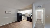 Located at 3246 S Holden Rd in Greensboro, NC, this single-floor residence offers a well-organized layout designed for comfortable everyday living. The kitchen is a standout feature, outfitted with crisp white shaker-style cabinetry, dark granite-look countertops, and a full suite of black appliances including a refrigerator, electric range, dishwasher, and range hood. Wood-style plank flooring runs throughout the main living areas, lending warmth and continuity to the space. The open connection between the kitchen and living area creates an airy, functional flow, with the living room benefiting from natural light through a front-facing window. A hallway leads to the private areas of the home, where the bedrooms feature neutral-toned walls, plush carpeting, and windows that bring in additional natural light and outdoor views. The bathroom is neatly appointed with a wide vanity topped with a white surface, shaker-style cabinetry below, a large wall mirror, and a tub-shower combination. Textured ceilings are present throughout, and the overall palette of soft grays, whites, and warm wood tones creates a clean, cohesive aesthetic that is both practical and inviting.