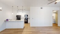 Located at 7300 N Silverbell Rd in Marana, AZ, this single-story, one-bedroom, one-bathroom unit offers a well-designed layout that maximizes every square foot. The open-concept living and dining area is anchored by light wood-style flooring, crisp white walls, and a ceiling fan, creating a bright and airy atmosphere. A sliding glass door leads to an outdoor balcony, filling the space with natural light. The dining area features a stylish pendant chandelier and a window with outdoor views. The kitchen is equipped with granite-style countertops, white shaker cabinetry extending to the ceiling, black appliances including a refrigerator, electric range, and built-in microwave, plus a peninsula with a sink that serves as a functional divide between the kitchen and dining space. The bedroom is carpeted, includes a ceiling fan, and receives natural light through a large window. A spacious walk-in closet with wrap-around shelving and hanging rods provides generous storage. The bathroom offers a full tub and shower combination with white tile surround, wood-style flooring, and brushed nickel fixtures. A dedicated in-unit laundry area accommodates a full-size washer and dryer side by side, adding everyday convenience to this thoughtfully appointed home.