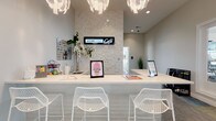 Located at 7027 Park Mill Dr in Plain City, Ohio, Jerome Grand Café is a thoughtfully designed single-floor café space that exudes a clean, modern aesthetic. The interior is anchored by a long, bright white service counter that serves as the focal point of the room, offering ample space for guest interaction and display. Complementing the counter are white lattice-style bar stools that add a decorative yet functional touch, inviting guests to sit and linger.

The back wall behind the counter is a standout architectural feature, clad in a textured three-dimensional tile that creates visual depth and interest against the otherwise minimalist white palette. Prominently displayed on this wall is the illuminated Jerome Grand Café signage, reinforcing the brand identity of the space.

Overhead, a pair of sculptural chandelier-style light fixtures with layered, petal-like detailing cast a warm, ambient glow throughout the space, elevating the overall atmosphere. Recessed ceiling lighting further enhances the brightness of the room, contributing to its airy and welcoming feel.

Decorative elements such as fresh white floral arrangements and colorful artwork add personality and warmth, balancing the crisp white surroundings. The overall ambiance is polished and inviting, making Jerome Grand Café a refined destination for community gathering and refreshment.