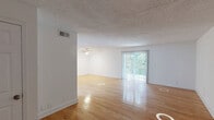 Located at 2700 Brigadoon Drive in Raleigh, NC, this single-floor, 2-bedroom, 1-bathroom home offers a comfortable and well-organized layout. Warm hardwood flooring flows throughout the main living areas and bedrooms, creating a cohesive and inviting aesthetic across the entire floor plan. The spacious living room is a standout feature, bathed in natural light from a large sliding glass door with vertical blinds that opens to an outdoor view of lush greenery. A ceiling fan overhead adds to the room's comfort and functionality. The kitchen is bright and practical, outfitted with white cabinetry, light countertops, and white appliances including a refrigerator and dishwasher. Light-toned flooring in the kitchen complements the clean, neutral palette throughout. Both bedrooms are generously sized with clean white walls and textured ceilings. The primary bedroom includes a built-in closet, while the second bedroom offers ample space and a window framing natural views. The full bathroom features subway tile in the shower/tub surround, updated fixtures with brushed brass accents, and wood-look flooring. A hallway connects the rooms efficiently, completing this well-appointed single-level home.