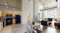 Located at 3201 First Ave in Columbus, GA, this one-bedroom, two-bathroom loft showcases an impressive industrial aesthetic with soaring ceilings, exposed white-painted brick walls, structural columns, and visible ductwork that pay homage to the building's architectural heritage. Polished concrete floors run throughout, complementing the open, airy feel of the space.

The open-concept main area seamlessly integrates the living room, dining room, and kitchen. The living room features exposed brick accents, including a distinctive arched brick detail, and benefits from large arched windows that flood the space with natural light. The kitchen is equipped with wood cabinetry and black appliances, while the dining area provides a central gathering space between the two zones.

The primary bedroom features the same dramatic ceiling height and a cozy, well-appointed layout. A secondary unclassified room, visible in the images with exposed brick, offers flexible use as a den or home office. Two full bathrooms serve the unit, one with warm wood vanity cabinetry and another with a tub/shower combination. Additional conveniences include in-unit laundry, two closets, and a hallway connecting the private quarters. This loft offers a compelling blend of historic character and modern livability.