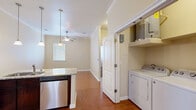 Located at 10800 McCombs St in El Paso, TX, this one-bedroom, one-bathroom unit offers a thoughtfully designed layout with functional living spaces across a single floor. The kitchen serves as a standout feature, showcasing rich dark wood cabinetry that extends to the ceiling, granite countertops, a tile backsplash, and a full suite of stainless steel appliances including a refrigerator, electric range, microwave, and dishwasher. A peninsula with pendant lighting opens the kitchen toward the living area, which features warm wood-look tile flooring, crown molding, and a ceiling fan. The bedroom is a comfortable, carpeted retreat with a ceiling fan, a window with blinds for natural light, and access to a walk-in closet outfitted with built-in shelving and hanging rods. The bathroom includes a full soaking tub with a tiled surround in earthy tones, complemented by wood-look tile flooring. A dedicated laundry area with a full-size washer and dryer adds everyday convenience. The warm, neutral color palette throughout creates a cohesive and inviting ambiance, making this unit a practical and comfortable home.