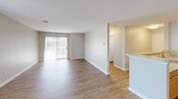 Located at 607 Windview Way in Frederick, Maryland, Unit 300 is a single-floor residence offering a clean, functional layout with consistent finishes throughout. The open living and dining area is a standout feature, showcasing warm wood-look flooring, neutral gray walls, and a large sliding glass door that invites an abundance of natural light while providing access to the outdoors. An additional window further brightens the space, creating an airy and welcoming atmosphere.

The galley-style kitchen is efficiently designed with warm-toned wood cabinetry, light granite-style countertops, a double-basin stainless steel sink, and black appliances including a refrigerator, range, and dishwasher. The kitchen connects seamlessly to the main living area via a peninsula counter, and a dedicated laundry closet with a stacked washer and dryer unit is conveniently accessible from the kitchen corridor.

The bathroom is well-appointed with matching wood cabinetry, granite-style countertops, wood-look flooring, a full tub-shower combination with white tile surround, and brushed nickel fixtures and hardware. A carpeted room, visible from the floorplan, offers a quieter, softer-floored space suitable for use as a bedroom. The unit's layout is thoughtfully arranged to maximize flow and utility throughout.