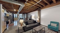 Located at 2001-19 Washington Ave in St. Louis, MO, this lower-level unit showcases a compelling blend of historic industrial architecture and contemporary functionality. The open-plan layout spans a generous single floor, unified by striking exposed wood beam ceilings with visible joists and original structural timber columns throughout. Polished concrete floors reflect light across the expansive living areas, contributing to the space's loft-like, industrial aesthetic.

The living area is spacious and versatile, accommodating multiple seating arrangements and defined zones. Original stone masonry walls add remarkable texture and historical character, particularly prominent in the bedroom area, where rough-cut stone meets a large window and warm, layered bedding. A movable partition wall provides flexible separation between the sleeping area and main living space.

The kitchen is efficiently designed with light maple cabinetry, stainless steel appliances including a range, microwave, refrigerator, and dishwasher, along with a double-basin sink, gray countertops, and a practical open shelving and hanging utensil rail system. The bathroom is clean and simply appointed. Exposed ductwork running along the ceiling reinforces the industrial character that defines this unique, historically rich St. Louis property.