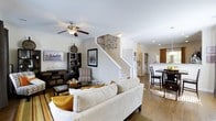 Located at 100 Durham Park Way in Pooler, Georgia, this two-story home offers a well-designed layout that balances comfort and functionality across both levels. The main floor showcases an open-concept floor plan where the living room, dining area, and kitchen flow naturally into one another, creating a spacious and inviting atmosphere. The living room is anchored by warm hardwood-style flooring and features a ceiling fan with light fixture, recessed lighting, and ample space for relaxed seating arrangements. A staircase with a clean white finish rises from the main living area, serving as a subtle architectural focal point while providing easy access to the upper level. The dining area is positioned adjacent to the kitchen and benefits from natural light streaming in through nearby windows, complemented by tasteful window treatments. The kitchen is visible from the main living space, reinforcing the home's open and connected feel. Crown molding details and neutral wall tones throughout the main level contribute to a bright, cohesive aesthetic. Built-in shelving and thoughtful storage solutions add practical character to the living spaces. The overall ambiance of the home is warm and welcoming, with a layout well-suited for both everyday living and entertaining.