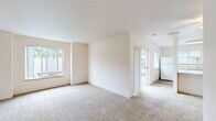 This single-floor, 2-bedroom, 2-bathroom residence offers a practical and comfortable layout designed for everyday living. The open living and dining area features neutral-toned carpet, warm beige walls, and multiple windows that allow generous natural light to fill the space. Sliding glass doors provide access to an outdoor area, further brightening the interior. The kitchen is well-equipped with ample white cabinetry accented by warm wood trim, a full suite of white appliances including a range, dishwasher, and refrigerator, and durable hardwood-style flooring. A window above the kitchen area adds additional natural light. The spacious primary bedroom offers plush carpeting, a large window with outdoor views, and access to a dedicated walk-in closet featuring wrap-around shelving and hanging rods for generous storage. The second bedroom is equally comfortable, with carpeted flooring, a window with vertical blinds, a baseboard heater, and convenient closet access. Both bathrooms are clean and functional, with one featuring a full tub-shower combo, a single vanity with integrated sink, and hardwood-style flooring. The space maintains a cohesive, neutral palette throughout, creating a bright and move-in-ready environment.
