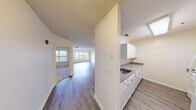 This well-appointed single-floor unit offers a clean, functional layout designed for comfortable everyday living. The open-concept living and dining area is a standout feature, finished with durable hardwood-style flooring that runs throughout the main living spaces, lending a cohesive and modern aesthetic. Natural light flows in generously through large windows, brightening the neutral-toned walls and contributing to an airy, welcoming ambiance. Track lighting in the living area provides additional illumination and a contemporary touch.

The kitchen is positioned adjacent to the main living space and features white cabinetry with brushed nickel hardware, a stainless steel sink, and dark granite-style countertops. Upper and lower cabinet storage offers practical organization, while a skylight adds natural brightness to the cooking area.

The bedroom is carpeted for comfort and includes a large window overlooking a balcony railing and green outdoor scenery, providing a tranquil retreat. The bathroom is finished with a full-size soaking tub and shower combination, complete with white subway tile surround and chrome fixtures, offering a clean and classic look.

Overall, the space presents a bright, neutral palette with consistent finishes throughout, making it a versatile and move-in-ready environment.