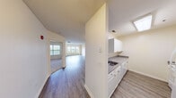 This well-appointed single-floor unit offers a clean, functional layout designed for comfortable everyday living. The open-concept living and dining area is a standout feature, finished with durable hardwood-style flooring that runs throughout the main living spaces, lending a cohesive and modern aesthetic. Natural light flows in generously through large windows, brightening the neutral-toned walls and contributing to an airy, welcoming ambiance. Track lighting in the living area provides additional illumination and a contemporary touch.

The kitchen is positioned adjacent to the main living space and features white cabinetry with brushed nickel hardware, a stainless steel sink, and dark granite-style countertops. Upper and lower cabinet storage offers practical organization, while a skylight adds natural brightness to the cooking area.

The bedroom is carpeted for comfort and includes a large window overlooking a balcony railing and green outdoor scenery, providing a tranquil retreat. The bathroom is finished with a full-size soaking tub and shower combination, complete with white subway tile surround and chrome fixtures, offering a clean and classic look.

Overall, the space presents a bright, neutral palette with consistent finishes throughout, making it a versatile and move-in-ready environment.