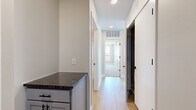 This single-floor residence offers a thoughtfully designed layout across a comfortable footprint, accommodating two bedrooms, two bathrooms, a combined kitchen and living area, a hallway, and two closets. The open-concept kitchen is a standout feature, showcasing grey shaker-style cabinetry, dark granite countertops, stainless steel appliances including a refrigerator, range, and built-in microwave, a peninsula with pendant lighting, and track lighting overhead. Light wood-style flooring runs throughout the main living and kitchen areas, contributing to a clean, contemporary aesthetic. The living area is bathed in natural light through large windows fitted with roller shades, offering views of the surrounding urban landscape. The primary bedroom features soft carpeting and a dedicated closet, while a second bedroom similarly offers carpeted flooring and a window with outdoor views. Both bathrooms are finished with grey vanity cabinetry and wood-look tile flooring; one includes a walk-in shower with chrome fixtures, while the other features a full tub-shower combination. Neutral wall tones and white trim throughout create a cohesive, modern ambiance.