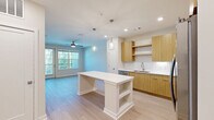 Located at 1153 Bees Ferry Rd on Johns Island, SC, this thoughtfully designed one-bedroom, one-bathroom residence offers a bright and modern living experience. The open-concept layout seamlessly connects the kitchen and living area, creating an inviting, cohesive space bathed in natural light. The kitchen is a standout feature, showcasing warm-toned flat-front cabinetry, white quartz countertops, subway tile backsplash, stainless steel appliances, and a central island with built-in shelving beneath sleek pendant lighting — ideal for both meal preparation and casual dining. Light hardwood-style flooring flows throughout the main living areas, complementing the clean, contemporary aesthetic. The living area opens directly to a private balcony through a glass-panel door, offering serene views of surrounding greenery, and is equipped with a ceiling fan for year-round comfort. The bedroom features plush carpeting, a ceiling fan, and a generous window with outdoor views. It connects to a spacious walk-in closet with wire shelving and a well-appointed bathroom, which includes a double-sink vanity with warm wood cabinetry, white countertops, and elegant pendant lighting. Recessed lighting throughout enhances the bright, airy ambiance of this well-designed residence.