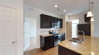 Located at The BLVD At Hays, this two-story home offers a thoughtfully designed layout with modern finishes throughout. The kitchen serves as a standout feature, showcasing rich dark cabinetry that contrasts beautifully with light granite countertops and a classic white subway tile backsplash. Stainless steel appliances, including an electric range, over-the-range microwave, and refrigerator, provide a sleek and functional cooking space. A double-basin sink is integrated into the island or peninsula, adding to the kitchen's practicality. Recessed lighting illuminates the space, while natural light flows in through windows, enhancing the open and airy feel. Durable hardwood-style flooring runs through the main living areas, adding warmth and easy maintenance. The home's two-floor layout offers a natural separation between living and private spaces, making it well-suited for a variety of lifestyles. Neutral wall tones and clean lines throughout contribute to a bright, move-in-ready atmosphere. The overall design balances contemporary style with everyday functionality, creating a welcoming environment at The BLVD At Hays community.