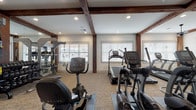 Located at 4140 Bayswater Rd in Winterville, NC, this single-floor fitness center is a comprehensively outfitted facility designed to support a wide range of workout routines. The space is characterized by its clean white walls, neutral carpet flooring, and striking exposed dark wood beam ceilings that lend a warm, upscale aesthetic throughout.

The main exercise floor houses a robust selection of TRUE-brand cardio equipment, including treadmills, ellipticals, and a recumbent bike, all arranged to maximize open floor space. A dedicated free weights area features a full dumbbell rack, kettlebells, TRX suspension trainers, an adjustable bench, and floor-to-ceiling mirrors that enhance both visibility and the sense of space. A multi-station cable machine and a Smith machine with an adjustable bench round out the strength training options.

A separate spin studio offers high-ceilinged, light-filled space with a row of spin bikes, wall-mounted TVs, and SmartPly plyo boxes for cross-training. Expansive windows with blinds line the walls throughout the facility, flooding the space with natural light and providing views of the surrounding community. Ceiling fans and recessed lighting ensure comfort during any workout.

An on-site restroom with accessibility features provides added convenience. The overall ambiance is modern, clean, and purposefully designed for an effective fitness experience.