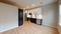 Located at 600 Willard St in Durham, NC, this single-floor unit offers a clean, contemporary design with light wood-tone flooring and neutral wall tones throughout. The open-concept kitchen is a standout feature, showcasing a bold two-tone design with crisp white upper cabinetry and dark lower cabinets, complemented by a white subway tile backsplash, light quartz countertops, and a full suite of stainless steel appliances including a refrigerator, range, microwave, and dishwasher. Recessed lighting illuminates the space efficiently.

The living area benefits from a large picture window that allows generous natural light to filter in while offering views of the surrounding urban streetscape. The bedroom is well-proportioned and includes a ceiling fan, ample natural light, and a set of paneled sliding closet doors providing convenient storage. A dedicated entry corridor features built-in hooks and shelving, offering a practical mudroom-style transition into the unit.

The full bathroom is finished with a clean, modern aesthetic, featuring white subway-tiled tub surround with matte black fixtures, a single vanity with white countertop, a bold black-framed mirror, and light tile flooring — creating a crisp, cohesive look throughout.