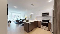 Located at 1177 Warburton Ave in Yonkers, NY, this modern single-floor residence offers a thoughtfully designed open-concept layout with clean lines and contemporary finishes throughout. Light-wood flooring flows seamlessly across the entire space, creating a bright and cohesive aesthetic.

The kitchen is a standout feature, equipped with stainless steel appliances, a full-height refrigerator, a subway tile backsplash, and a two-tone cabinetry design combining gloss white uppers with wood-grain lowers. A peninsula with bar seating and pendant lighting serves as the centerpiece, opening directly to the dining and living areas.

The living room is generously proportioned, bathed in natural light from floor-to-ceiling sliding glass doors that lead to a private balcony with green outdoor views. The dining area integrates naturally within this open space, ideal for entertaining.

The primary bedroom offers a ceiling fan, large windows with outdoor views, and ample natural light, while the second bedroom is a comfortable and well-appointed space with a sizable closet. A spacious walk-in closet with built-in wire shelving and dedicated shelf units provides exceptional storage.

Two bathrooms serve the residence — one featuring a wood-grain vanity, white quartz countertop, and tiled shower, and the other offering a soaking tub with a curved shower rod and clean white tile surround.