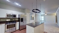 This single-story, 2-bedroom, 2-bathroom residence offers a practical and cohesive layout across its efficiently designed floor plan. The kitchen serves as a standout feature, equipped with stainless steel appliances including a French door refrigerator, range, microwave, and dishwasher. White shaker-style cabinetry pairs with dark granite countertops, and a central island provides additional prep space. A distinctive chain-hung pot rack is suspended overhead, adding a functional yet stylish touch. Hardwood-style flooring runs throughout the kitchen and living areas, while track lighting enhances visibility. The living area connects seamlessly to the kitchen, featuring crown molding and a ceiling fan. Both bedrooms are carpeted and include ceiling fans with light fixtures. The primary bedroom is generously proportioned, featuring built-in shelving, a ceiling fan, and access to a dedicated closet. Each bathroom includes a tub-shower combination with white tile surround, with one bathroom featuring a granite-top vanity with white cabinetry and direct access to an adjacent walk-in closet with built-in shelving. Neutral gray tones throughout create a calm, consistent ambiance.