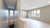 This single-floor home showcases a clean, modern design highlighted by a consistent palette of soft gray walls, warm natural wood trim, and light hardwood-style flooring throughout. The open-concept kitchen serves as a central hub, featuring natural maple cabinetry, a subway tile backsplash, stainless steel appliances including a gas range and French door refrigerator, and a large island with a white quartz countertop and undermount sink. Stylish pendant lighting adds a contemporary touch above the island. The living area is bright and airy, benefiting from multiple large windows with natural wood frames that invite abundant natural light and offer views of the surrounding neighborhood. Recessed lighting throughout ensures consistent illumination. The bedroom spaces are generously proportioned, each with light hardwood flooring, recessed lighting, and wood-framed windows that frame outdoor views. One room features a ceiling fan for added comfort. The bathroom is well-finished, with natural maple vanity cabinetry, a white quartz countertop, brushed nickel fixtures, and a framed mirror. A dedicated laundry room provides added convenience, housing a full-size washer and dryer. Throughout the home, cohesive finishes and quality craftsmanship create a warm, inviting atmosphere.