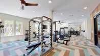 Located at 14355 N Main St in Jacksonville, FL, this single-floor fitness center offers a generously sized, thoughtfully designed workout facility divided into two distinct areas. The main gym area is outfitted with an extensive array of equipment, including power racks, cable machines, weight benches, a full dumbbell rack, and multiple treadmills and cardio machines, catering to a wide range of fitness routines. Ceiling fans and recessed lighting keep the space comfortable and well-lit, while multiple windows along the walls usher in abundant natural light and views of the outdoors. Full-length mirrors are strategically placed throughout, amplifying the sense of space and supporting proper form during workouts. The secondary room serves as a dedicated studio space, featuring the same striking geometric-patterned carpet in teal, brown, and neutral tones, floor-to-ceiling mirrors, and additional equipment such as medicine balls and resistance tools. A water fountain station with tiled accent walls and a wood-paneled entryway add refined touches to the facility. The overall ambiance is bright, modern, and energizing, making it a well-rounded fitness destination.