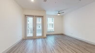 This single-story unit is thoughtfully designed with a clean, contemporary aesthetic throughout. Light-toned wood-look flooring flows continuously across the open living and kitchen areas, creating a cohesive and airy feel. The living space is brightened by natural light from multiple windows fitted with blinds, complemented by a ceiling fan with integrated lighting. A set of glass French doors provides access to an outdoor area, further enhancing the sense of openness.

The kitchen is a functional highlight, featuring rich dark-espresso cabinetry that contrasts sharply with light granite countertops. A stainless steel suite of appliances—including a refrigerator, electric range, over-the-range microwave, and dishwasher—lines the kitchen wall, finished with a distinctive geometric-patterned tile backsplash and an under-mount sink with a modern brushed-nickel faucet.

The bedroom offers ample natural light and ceiling fan, with access to a spacious walk-in closet fitted with mirrored sliding doors and built-in shelving. The bathroom is well-appointed with large-format gray tile surrounding the soaking tub and shower, white tile flooring, dark cabinetry with granite countertops, and brushed-nickel fixtures throughout.