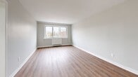 This 430 square foot apartment offers a thoughtful blend of comfort and functionality in a compact urban setting. The space is efficiently designed with one bedroom, one bathroom, and an open-concept living area. Light wood-tone flooring runs throughout, creating a seamless flow and enhancing the sense of space.

The living room is bright and airy, featuring a large triple-pane window that floods the area with natural light and provides views of the surrounding cityscape. A baseboard heater beneath the window ensures comfort year-round. The room's neutral palette and clean lines create a versatile canvas for personal styling.

The bedroom, measuring 110 square feet, continues the apartment's minimalist aesthetic with ample floor space and a window that invites natural light. A compact radiator provides targeted heating for the space.

The bathroom is well-appointed with modern fixtures, including a vanity with storage, a large mirror, and a shower-tub combination. Light-colored tiles on the walls and floor contribute to a clean, spacious feel.

The apartment's layout includes a practical hallway that connects the living spaces, optimizing the compact floor plan. While not visible in the images, the kitchen area is likely integrated into the open-concept design, completing this efficient urban living space.