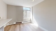 Located at 280 Dundas Street East in Toronto's vibrant downtown east neighbourhood, this compact single-floor unit offers an efficient and well-organized layout. Light-toned laminate flooring runs throughout, lending a clean, cohesive look to the entire space.

The entry hallway provides a welcoming transition into the unit, with recessed lighting overhead and a closet for storage. The kitchenette is thoughtfully designed, featuring white shaker-style upper and lower cabinetry with gold-toned hardware, a white refrigerator, microwave, and an extended countertop that offers ample workspace. The light-coloured counters and neutral walls keep the area feeling bright and functional.

The main living area benefits from a large corner window that draws in generous natural light and frames views of surrounding greenery. Neutral grey walls, light laminate flooring, and a baseboard heating unit complete the room, creating a simple and adaptable space.

The bathroom is finished with white subway-style tile in the tub and shower surround, complemented by chrome fixtures, maintaining the clean and minimal aesthetic consistent throughout the unit. Overall, this space presents a practical and modern interior well-suited to its urban Toronto location.
