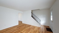 This thoughtfully designed multi-level space unfolds across three floors, offering a versatile and well-structured layout. The main level immediately impresses with its warm, light-toned hardwood flooring that runs throughout, creating a cohesive and inviting atmosphere. Bright white walls reflect natural light and lend a clean, modern aesthetic to the interior.

A standout architectural feature is the staircase, framed by sleek wrought iron railings that add a touch of industrial elegance to the otherwise minimalist design. The staircase serves as both a functional and visual centerpiece, connecting the three levels in a stylish manner.

The open, airy feel of the main living area is complemented by a connected room accessible through a doorway, suggesting a flexible floor plan suited to a variety of uses. Baseboard heating is visible along the walls, providing practical climate control throughout the space.

The clean lines, neutral color palette, and consistent hardwood flooring across the levels create a unified sense of flow from floor to floor. The overall ambiance is bright, calm, and understated — a well-maintained space that offers a solid foundation for any number of configurations or furnishing styles.