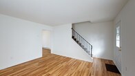 This thoughtfully designed multi-level space unfolds across three floors, offering a versatile and well-structured layout. The main level immediately impresses with its warm, light-toned hardwood flooring that runs throughout, creating a cohesive and inviting atmosphere. Bright white walls reflect natural light and lend a clean, modern aesthetic to the interior.

A standout architectural feature is the staircase, framed by sleek wrought iron railings that add a touch of industrial elegance to the otherwise minimalist design. The staircase serves as both a functional and visual centerpiece, connecting the three levels in a stylish manner.

The open, airy feel of the main living area is complemented by a connected room accessible through a doorway, suggesting a flexible floor plan suited to a variety of uses. Baseboard heating is visible along the walls, providing practical climate control throughout the space.

The clean lines, neutral color palette, and consistent hardwood flooring across the levels create a unified sense of flow from floor to floor. The overall ambiance is bright, calm, and understated — a well-maintained space that offers a solid foundation for any number of configurations or furnishing styles.
