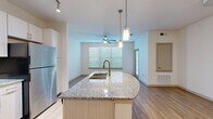 This thoughtfully designed 1-bedroom, 1-bathroom residence offers a functional and modern living experience across a single floor. The open-concept layout seamlessly connects the kitchen, dining, and living areas, creating a cohesive and airy atmosphere brightened by multiple windows with blinds that invite natural light throughout.

The kitchen is a standout feature, anchored by a curved granite-topped island with a brushed gold undermount sink and pendant lighting overhead. White cabinetry lines the walls alongside a full suite of stainless steel appliances, including a refrigerator, electric range, and microwave. Track lighting above enhances both functionality and ambiance.

The living area flows naturally from the kitchen, complete with a ceiling fan and large windows that frame views of the outdoors. Wood-look flooring runs throughout the entire unit, providing a warm and consistent aesthetic.

The generously sized primary bedroom features a ceiling fan, a large window for natural light, and direct access to a spacious walk-in closet outfitted with wire shelving on three walls for ample storage.

The bathroom is clean and efficient, featuring a framed glass walk-in shower with tile surround, a granite-topped vanity with wood cabinetry, and tile flooring. Two hallways connect the living spaces to the private areas of the unit, ensuring a well-organized and practical floor plan throughout.