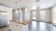 Located at 1805 S Bannock St in Denver's vibrant Baker neighborhood, this well-appointed single-floor unit offers a thoughtfully designed open layout. The combined kitchen and living area serves as the heart of the space, where a sleek kitchen island with a warm countertop anchors the room. The kitchen is outfitted with white shaker-style cabinetry reaching toward the ceiling, a classic subway tile backsplash, and a full suite of stainless steel appliances, including a French door refrigerator, electric range, built-in microwave, and dishwasher. Pendant lighting and a track light fixture add warmth and functionality overhead. Durable wood-look flooring flows seamlessly throughout the entire unit, tying each area together cohesively. The living area benefits from multiple large windows fitted with horizontal blinds, inviting an abundance of natural light and offering views of the surrounding neighborhood. A ceiling fan provides added comfort year-round. The bathroom features a white vanity with a dark wood-toned countertop, a framed mirror, and consistent wood-look flooring. A generously sized walk-in closet with multi-level shelving and hanging rods provides ample storage. Clean lines, neutral tones, and modern fixtures define the overall aesthetic of this Denver residence.