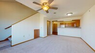 Located at 2125 McComb Rd in Stoughton, Wisconsin, this two-story residence offers a well-organized layout spread across two levels connected by a wood-railed staircase. The main level features a generously sized living area with plush carpeting, warm neutral walls, and a ceiling fan that provides both comfort and ambiance. The open flow leads directly into the kitchen, which is equipped with warm honey-toned cabinetry, dark granite-style countertops, hardwood flooring, and a full suite of white appliances including a refrigerator, range, microwave, and dishwasher — all arranged in a functional U-shaped layout. A full bathroom on the main level includes a tub/shower combination, a single-sink vanity with wood cabinetry, and tile flooring. A second half-bathroom provides additional convenience and features matching wood cabinetry and tile floors. The upper level offers a spacious loft-style area with sloped ceilings, plush carpeting, and an exterior door that opens to an outdoor balcony or landing, providing natural light and outdoor views. This flexible upper space is well-suited for a variety of uses. Throughout the home, consistent wood trim accents, neutral tones, and practical finishes create a cohesive and comfortable living environment.