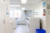 Located at 222 Nonquon Rd in Oshawa, Ontario, this shared laundry facility is a well-equipped, single-floor space designed to serve the practical needs of its users. The room features white ceramic tile flooring throughout, which contributes to a clean, uniform aesthetic that is easy to maintain. A suspended drop ceiling with integrated fluorescent lighting ensures the space is consistently and evenly lit.

The facility is lined on both sides with rows of commercial-grade front-loading washing machines and top-loading dryers, providing ample laundry capacity. The machines are clearly numbered for easy identification, and informational signage is posted throughout to guide users on proper operation and available payment systems. A dedicated utility sink station is also present, offering additional functionality for hand-washing or pre-treating garments.

Natural light filters in through windows positioned along one wall, lending a degree of brightness to the otherwise utilitarian space. A bulletin board mounted on the wall serves as a central communication point for notices and community information. A small seating area with a chair is available, allowing users to wait comfortably. A secondary door provides additional access to the room. Overall, the space is straightforward, practical, and efficiently organized to accommodate shared laundry use.