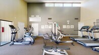 Located at 10139 Woodley Avenue in North Hills, CA, this fitness center is a compact yet thoughtfully outfitted facility designed to support a well-rounded workout routine. The space spans a single floor and is organized to maximize usability, with equipment arranged to allow comfortable movement throughout.

The facility features soaring vaulted ceilings that lend an open, airy feel to the room, preventing any sense of confinement despite its modest footprint. Natural light floods the interior through a row of clerestory windows positioned near the top of the walls, as well as through large sliding glass doors that provide direct access to an outdoor patio or courtyard area. The neutral-toned walls and patterned carpet flooring contribute to a clean, functional aesthetic.

Cardio equipment is well represented, with multiple treadmills, elliptical trainers, a stationary bike, and a rowing machine available for use. Strength training is supported by a multi-station cable machine, adjustable benches, and additional resistance equipment. A wall-mounted mirror enhances the sense of space and allows users to monitor their form. Safety essentials, including a fire extinguisher and hand sanitizer dispenser, are also present. An adjoining room provides additional utility to the overall facility.