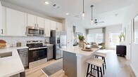 This thoughtfully designed one-bedroom, one-bathroom residence offers a cohesive blend of modern style and functional living across a single floor. The open-concept kitchen and living area serves as the heart of the home, anchored by a central island with a crisp white quartz countertop and bar seating. The kitchen is equipped with stainless steel appliances, two-tone cabinetry featuring white upper cabinets and gray lower cabinets, a classic subway tile backsplash, and light wood-style flooring that flows throughout. Pendant lighting above the island adds a polished finishing touch. The adjoining living room is bright and welcoming, with multiple windows dressed in layered blinds and sheer curtains that allow abundant natural light. A ceiling fan enhances comfort, and the space opens to a private outdoor area with a patio and a small patch of lawn. The generously sized bedroom offers a serene retreat with large windows, a ceiling fan, and continued wood-style flooring. The full bathroom features gray vanity cabinetry with a white countertop, a tub-shower combination, and light wood flooring, all finished with sleek matte black hardware accents throughout.