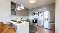 This modern residence in Chula Vista, CA offers three bedrooms, two bathrooms, and a thoughtfully designed layout across one living floor. The open-concept kitchen is a standout feature, showcasing high-gloss gray cabinetry that extends to the ceiling, a white quartz waterfall island with bar seating, stainless steel appliances, a subway tile backsplash, and stylish pendant lighting — all set over warm hardwood-style flooring. The living room impresses with floor-to-ceiling glass windows and sliding doors that flood the space with natural light and frame expansive outdoor views, complemented by a ceiling fan overhead. The primary bedroom features corner windows with sweeping views, while the additional bedrooms offer generous closet space and warm, neutral finishes. Both bathrooms are finished with marble-style tile surrounds — one featuring a glass-enclosed walk-in shower with a wood-tone vanity and white quartz countertop, and the other a full soaking tub and shower combination. A dedicated in-unit laundry closet with a stacked washer and dryer adds everyday convenience. Throughout, the space maintains a clean, contemporary aesthetic with consistent hardwood-style flooring and a light, airy ambiance.