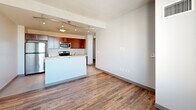 Located at 10 Commerce Ave SW in the heart of downtown Grand Rapids, Michigan, this one-bedroom, one-bathroom unit offers a well-planned layout across a single floor. Wood-style plank flooring runs throughout the main living areas, lending warmth and continuity to the space.

The open-concept living area flows directly into a compact kitchen equipped with rich, warm-toned cabinetry, stainless steel appliances including a range and microwave, and a peninsula with a breakfast bar — all illuminated by a track lighting system overhead. The layout makes efficient use of the available footprint, keeping the space functional and connected.

The bedroom offers a cozy yet practical retreat, featuring a window with city views of the Grand Rapids skyline, providing natural light and an urban backdrop. Exposed concrete structural columns add an industrial character that complements the modern aesthetic. A dedicated closet provides built-in storage.

The hallway connects the living and private areas cleanly, with recessed lighting maintaining a bright, neutral atmosphere. The bathroom is finished with large-format grey tile flooring, dark wood cabinetry with an integrated sink, and a full tub and shower combination with dark tile surround — a clean and functional design throughout. This unit is well-suited for those seeking contemporary urban living in downtown Grand Rapids.