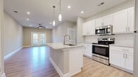 Located at 8000 Carlow Dr in Kernersville, NC, this single-floor residence offers a thoughtfully designed layout with 2 bedrooms and 2 bathrooms. The open-concept kitchen and living area serves as the heart of the home, showcasing light hardwood-style flooring, recessed lighting, and elegant pendant lights above a granite-topped central island with an undermount sink. White shaker cabinetry, a subway tile backsplash, and stainless steel appliances — including a range, microwave, and refrigerator — complete the kitchen. The living room flows seamlessly from the kitchen, featuring a ceiling fan and a set of French doors that invite natural light and provide outdoor access. Both bedrooms are carpeted and offer natural light through slatted blinds, with the primary bedroom connected to its own en-suite bathroom. The bathrooms feature granite vanity countertops, white cabinetry, and tile flooring. A spacious walk-in closet with built-in wire shelving and a natural light window adds practical storage. The dedicated laundry room includes washer and dryer hookups. Neutral wall tones and clean white trim throughout create a cohesive, modern aesthetic.