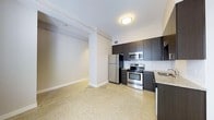 This single-floor space offers a clean, contemporary design that blends functionality with modern style. The kitchen is a standout feature, outfitted with stainless steel appliances including a refrigerator, range with oven, and microwave. Dark espresso-toned cabinetry contrasts elegantly against a classic white subway tile backsplash, while granite countertops add a refined finish. The sink area is neatly integrated into the cabinetry layout, maximizing workspace efficiency. The flooring throughout is a distinctive terrazzo, offering both durability and a timeless aesthetic that ties the space together. The open layout between the kitchen and the adjacent living area creates a seamless flow, making the space feel expansive and inviting. Neutral white walls and flush-mount ceiling lighting keep the interior bright and airy. Structural column details add an architectural character to the space, while the wide baseboards provide a polished, finished look. The overall ambiance is modern and minimalist, making it a versatile space well-suited for a variety of uses.