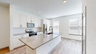 This three-floor home in Wyoming, Michigan offers a clean, contemporary design with light wood-look flooring and a bright, neutral palette carried throughout. The main living level features an open-concept kitchen and living room that serves as the heart of the home. The kitchen is outfitted with crisp white shaker cabinetry, subway tile backsplash, stainless steel appliances, and a large center island with a quartz-style countertop and undermount sink with a matte black faucet — ideal for both cooking and casual dining. The adjacent living area receives generous natural light through multiple windows and features a ceiling fan and French doors that open to an outdoor space, enhancing the airy feel. Three bedrooms are distributed across the upper floors, each featuring light flooring, ceiling fans, and well-sized windows that bring in views of the surrounding greenery. The spacious primary bedroom includes an en-suite with white cabinetry, quartz countertops, and black hardware accents. Five bathrooms in total are finished consistently with white subway tile tub surrounds, wood-look flooring, and matte black fixtures. A hallway with walk-in closet access adds practical storage. Recessed lighting throughout and a cohesive modern aesthetic make this a well-appointed, move-in-ready home.