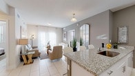 This well-designed single-floor residence offers a cohesive, light-filled interior finished throughout in a neutral palette of whites and soft grays. Large-format porcelain tile flooring flows seamlessly across the main living areas, enhancing the sense of openness throughout.

The open-concept layout connects the kitchen, dining, and living areas into one fluid space. The kitchen features a granite-topped breakfast bar with seating, white cabinetry, and white appliances, complemented by warm taupe accent walls. A glass-top dining table sits adjacent to the entry, which is appointed with a full-length mirror and console.

The living room is bright and airy, with floor-to-ceiling sheer curtains framing a sliding glass door that invites abundant natural light. A glass coffee table and plush sofa anchor the space beneath a large statement artwork.

The primary bedroom is serene and well-lit, featuring vertical blinds on a large window, tile flooring, and ample space for a dresser and nightstands. A generous walk-in closet with wire shelving provides practical storage. The second bedroom is equally bright, benefiting from dual windows and a ceiling fan.

The bathroom presents a refined vanity with a granite countertop, an undermount sink, and a wood-toned cabinet, paired with large-format tile flooring and a well-lit mirror arrangement.