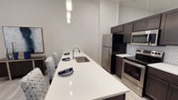 This single-floor residence showcases a contemporary design with a neutral color palette and light wood-style flooring throughout the main living areas. The kitchen is a standout feature, offering dark espresso cabinetry paired with crisp white quartz countertops, a full suite of stainless steel appliances including a refrigerator, electric range, and built-in microwave, and a geometric patterned tile backsplash that adds visual interest. An extended kitchen island with an undermount sink provides additional workspace and doubles as a casual dining area, illuminated by stylish pendant lighting overhead. Recessed lighting further brightens the space.

The bedrooms are carpeted and finished in soft gray tones, creating a calm, restful atmosphere. Each room offers functional layout space and access to well-appointed bathrooms. One bathroom features a glass-enclosed walk-in shower with large-format marble-style tile, while the second includes a soaking tub and tub surround tiling, both complemented by dark vanity cabinetry and light countertops.

The living area benefits from a large window that allows natural light to filter in, creating a warm and inviting atmosphere suited for relaxing or entertaining.