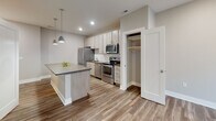 Located at 3020 Leavenworth St in Omaha, Nebraska, this single-floor residence showcases a clean, modern design with an open-concept layout that promotes a seamless flow between living spaces. The kitchen is a standout feature, equipped with stainless steel appliances including a refrigerator, electric range, and built-in microwave. Light wood-toned cabinetry with sleek hardware lines the walls above a classic white subway tile backsplash, while a generously sized island with a quartz-style countertop provides additional workspace and casual seating. Pendant lighting overhead adds a refined touch to the kitchen area. Wood-look plank flooring extends throughout the main living area, contributing warmth and continuity to the space. The living area connects directly to a private balcony through a large sliding glass door, filling the room with natural light and offering views of the surrounding exterior. The bedroom is carpeted and features a large window, further enhancing the natural brightness of the space. The bathroom is appointed with a wood-toned vanity, a framed mirror, white quartz countertop, and a full tub-shower combination. A dedicated closet and in-unit washer and dryer hookups, visible in the floorplan, add practical convenience to this well-designed residence.
