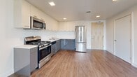 This studio at 3240 Hollis St in Oakland, California offers a well-designed single-floor layout that includes a living area, kitchen, bathroom, and closet. The living area is bright and open, featuring warm wood-tone laminate flooring and large windows fitted with blinds that allow abundant natural light while offering views of the surrounding neighborhood and greenery. The clean white walls and neutral palette create a calm, modern atmosphere throughout.

The kitchen is thoughtfully appointed with two-tone cabinetry — crisp white upper cabinets and gray lower cabinets — paired with stainless steel appliances including a gas range, microwave, dishwasher, and a full-size refrigerator. Recessed lighting illuminates the workspace, and the layout makes efficient use of the available area.

The bathroom is clean and functional, featuring a tub and shower combination with a glass curtain rod, wood-tone flooring, and white walls that give the space a fresh, minimalist feel. Grab bars are also present, adding a practical accessibility feature.

Throughout the studio, the consistent use of light wood-tone flooring, white walls, and modern finishes creates a cohesive and inviting aesthetic. A dedicated closet provides essential storage. The multiple windows ensure the space feels open and connected to the outdoors.