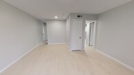 Unit #14 is a well-appointed 2-bedroom, 1-bathroom residence laid out entirely on a single floor, offering a clean and modern aesthetic throughout. The living area welcomes residents with light-toned laminate flooring, soft gray walls, and recessed lighting, creating a bright and open atmosphere. A front entry door with an arched transom window and an adjacent large window invite natural light into the main living space, enhancing its airy feel.

The kitchen features white raised-panel cabinetry, granite-look countertops, a subway tile backsplash, and stainless steel fixtures including a undermount sink and gas range. Open wood shelving adds a contemporary touch and provides additional storage.

Both bedrooms are finished with the same light laminate flooring and neutral gray walls. The primary bedroom is generously proportioned with a closet and multiple access points. The second bedroom includes a window with blinds for natural light and a closet with built-in shelving. The shared full bathroom is finished with white tile surrounding a tub/shower combination, chrome fixtures, and a window for ventilation and natural light. Clean white trim and consistent finishes tie the entire unit together for a cohesive, move-in-ready look.