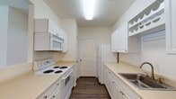 This single-floor unit offers a practical and comfortable layout designed for everyday living. The open living area features warm hardwood-style flooring and a ceiling fan with a light fixture, creating a bright and airy atmosphere. A pass-through window connects the living space to the kitchen, while an adjacent dining area is highlighted by a stylish pendant light overhead.

The galley-style kitchen is efficiently designed with white cabinetry, light countertops, a full suite of white appliances including a range, microwave, and refrigerator, plus a stainless steel sink. A built-in wine rack adds a thoughtful design detail, and the dark hardwood-style flooring ties the space together neatly.

The bedrooms are carpeted for comfort, with ceiling fans providing additional airflow. Natural light filters in through windows with blinds, and each bedroom benefits from closet access. One bedroom features a door leading to an outdoor area.

The bathrooms are clean and functional. The full bathroom includes a tub-shower combination, vanity with a single sink, a large mirror, and hardwood-style flooring. A second bathroom offers a more compact layout with similar finishes. Throughout the unit, white panel doors, neutral walls, and consistent flooring choices create a cohesive and move-in ready environment.