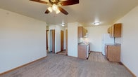 This single-floor residential unit offers a practical and well-organized layout designed for comfortable everyday living. The open living area serves as the heart of the unit, featuring plush carpeting, neutral-toned walls, and a ceiling fan with integrated lighting that ensures year-round comfort. A sliding glass door leads directly to a private balcony, filling the space with natural light and providing outdoor views.

The kitchen is positioned adjacent to the living area and is outfitted with warm wood-toned cabinetry, granite-pattern countertops, a stainless steel sink, and a full suite of white appliances including a coil-burner range, over-the-range microwave, and refrigerator. Light wood-look flooring in the kitchen provides a clean contrast to the carpeted living spaces.

The bedroom is a quiet, carpeted retreat with a window that frames outdoor views and allows ample natural light to flow through. The full bathroom is clean and straightforward, featuring a tub-shower combination, a toilet, and tile flooring in a neutral palette. A hallway connects the main areas, with additional closet and storage access visible throughout. Overall, the unit presents a tidy, functional design with consistent finishes throughout.