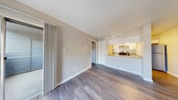 This single-floor unit offers a practical and well-appointed layout that flows seamlessly from one area to the next. The open-concept design connects the kitchen and living area, creating a sense of openness and ease of movement. The kitchen is outfitted with white cabinetry, granite-style countertops, a subway tile backsplash, a stainless steel electric range with a ventilation hood, and a stainless steel refrigerator. A half-wall peninsula separates the kitchen from the living space, offering convenient pass-through access and additional counter seating. The living area is generously sized, featuring wood-look plank flooring that extends throughout the unit, neutral-toned walls, and a textured ceiling. A sliding glass door opens to a balcony, allowing natural light to pour into the space. The bedroom is a comfortable, well-proportioned room with the same warm wood-look flooring and ample wall space. The bathroom is neatly designed with a tiled tub-shower surround, a white vanity with granite-style countertop, and matching wood-look flooring. The overall ambiance is clean, modern, and move-in ready, with a cohesive neutral palette that lends itself well to a variety of interior styles.
